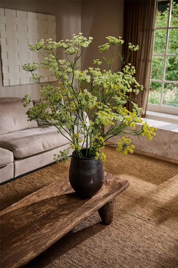This image displays an elegant and minimalist arrangement of high-quality silk flowers from the Silk-ka brand. The delicate green and yellow tones of the flowers are beautifully complemented by the natural wooden table and cozy interior. The realism of the silk flowers is so striking that it brings a fresh, lively atmosphere to the space, demonstrating Silk-ka's exceptional craftsmanship and attention to detail.