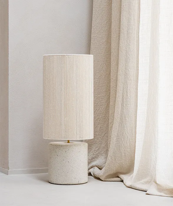 Elegant Mon Dada table lamp from Belgium. Features a minimalist cylindrical base crafted from speckled off-white concrete, topped with a sleek cream-colored fabric shade. The lamp embodies Mon Dada's signature blend of raw materials and refined design. Set against a neutral backdrop, it showcases the brand's commitment to timeless, sustainable luxury in home decor.