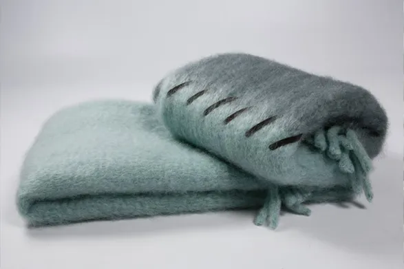 A luxurious blanket from the 'Stitching' collection by Mantas Ezcaray, a renowned Spanish brand known for its artisanal craftsmanship. The blanket, shown in a soft, elegant shade of green, is crafted with exquisite attention to detail, featuring a plush texture and delicate stitching. Mantas Ezcaray, with its rich heritage dating back to the 1930s, continues to create timeless pieces that blend traditional techniques with contemporary design, making this blanket a beautiful and sophisticated addition to any home.
