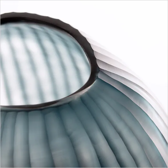 Close-up view of a Guaxs glass vase with a captivating wave-like texture in a soothing blue hue. The intricate detailing and smooth curves reflect the brand's dedication to producing exquisite, high-quality glassware. Each Guaxs piece is handblown by skilled master glassblowers, ensuring a unique blend of contemporary design and timeless elegance.