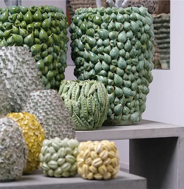 Exquisite handcrafted vases by Dutch brand Des Pots. Large green vases adorned with intricate fig and leaf patterns stand proudly on display. Smaller vases in various shades showcase unique textures and designs. These artisanal pieces blend natural motifs with contemporary elegance, creating stunning focal points for any interior.