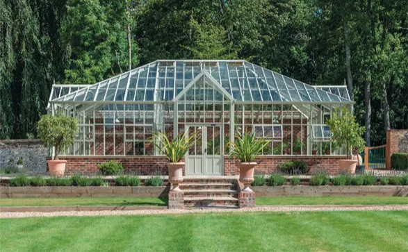 Exquisite Hartley Botanic greenhouse, a masterpiece of Victorian-inspired design set against lush greenery. The gleaming glass structure, supported by an elegant white frame, showcases the brand's commitment to perfect design and enduring strength. With its brick base and symmetrical layout, this greenhouse embodies Hartley Botanic's 30-year guarantee of unparalleled quality and everlasting performance, promising a lifetime of horticultural excellence.